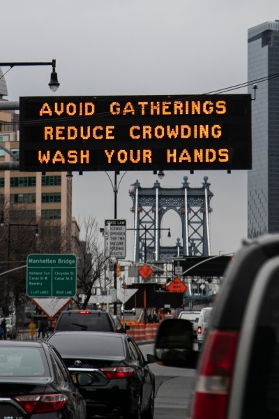 The Manhattan bridge is seen in the background of a flashing sign urging commuters to avoid gatherings, reduce crowding and to wash hands in the Brooklyn borough of New York