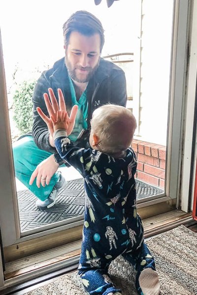 Dr. Jared Burks, sees his 1-year-old son crawl for the first time, as he touches a glass door from the outside while their son Zeke touches it from the inside of their Jonesboro, Ark.