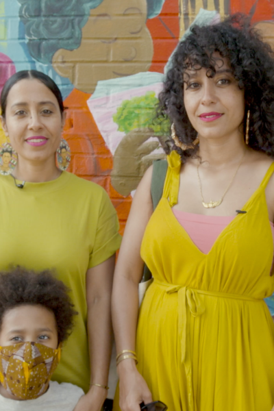 Two women wearing yellow stand in front of a mural with a child.