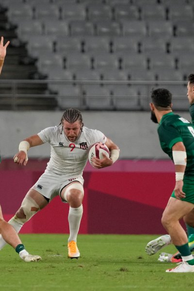 Steve Tomasin of the United States carries the ball through a cluster of players from Ireland in their men's rugby sevens match at the 2020 Summer Olympics
