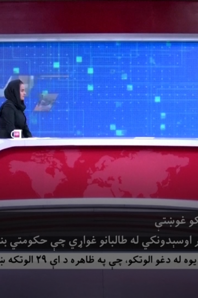 Female news anchor at desk with Taliban spokesman