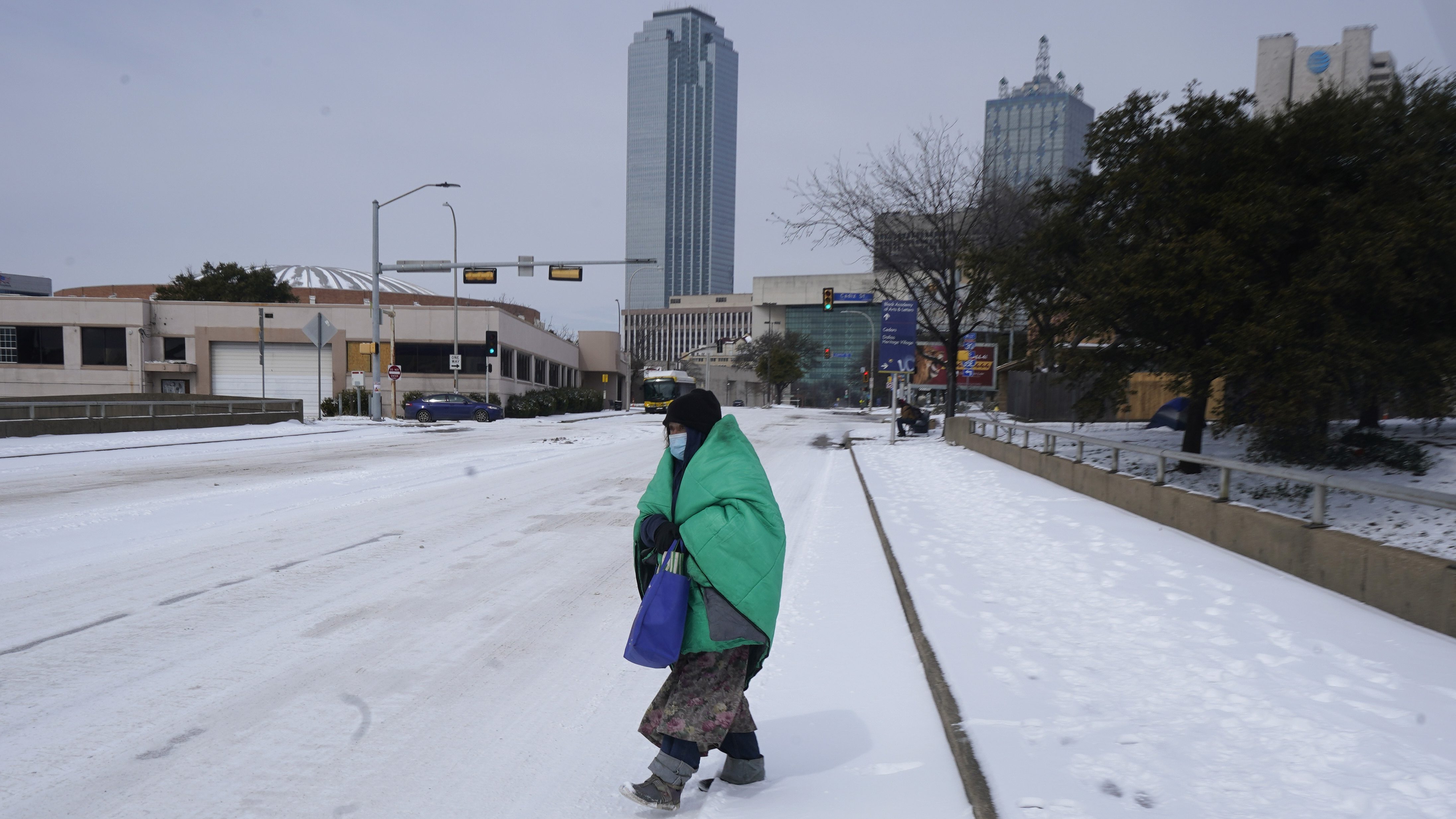 A woman wrapped in a blanket crosses the street near downtown Dallas, Feb. 16, 2021. Much of Texas' power grid collapsed, followed by its water systems, as temperatures plunged and snow and ice whipped the state.