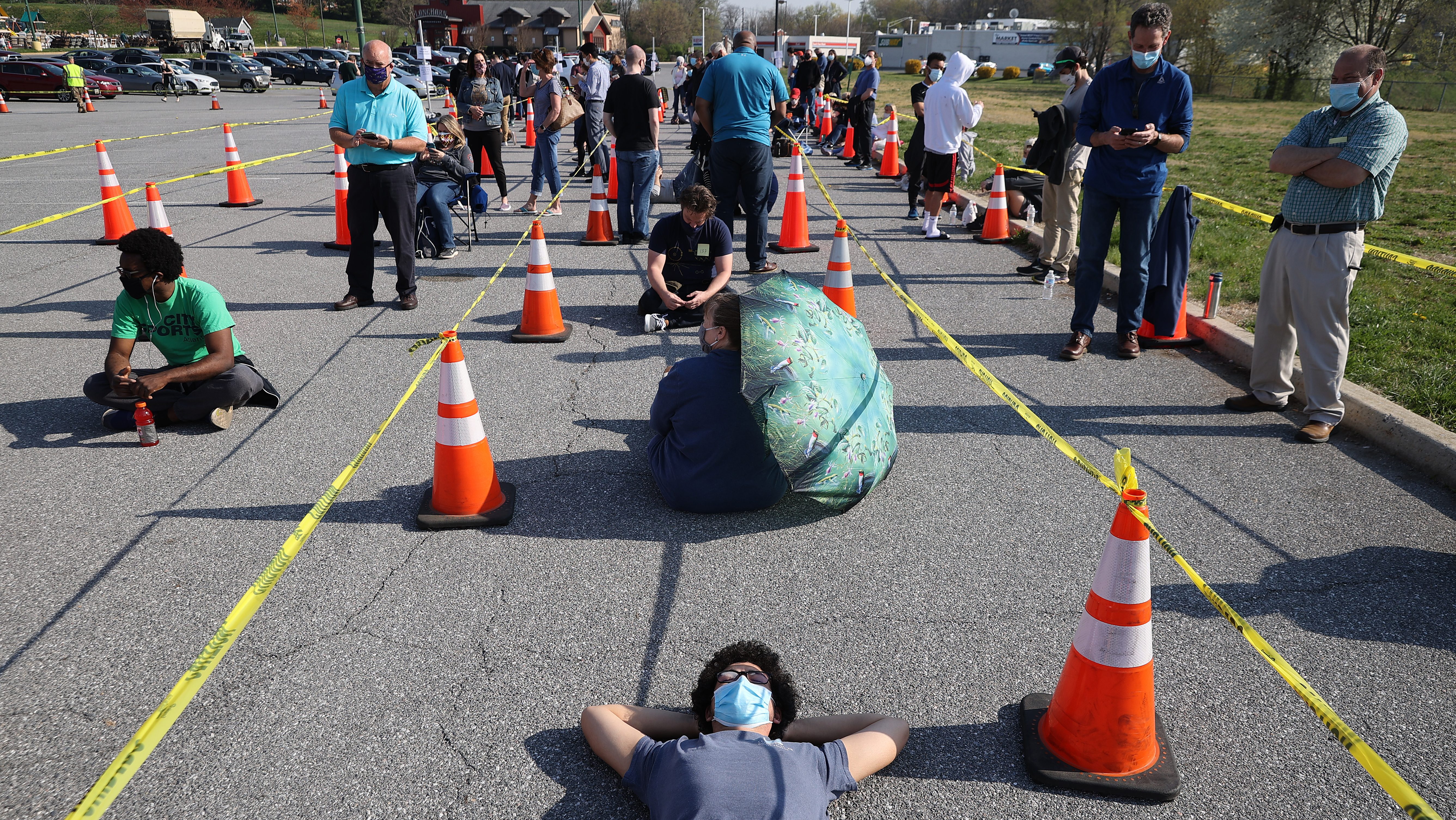 Eugene Chirkov of Bethesda, Maryland, finds a sliver of shade from a traffic cone while waiting in line with people without appointments outside the mass coronavirus vaccination site at Hagerstown Premium Outlets on April 7, 2021, in Hagerstown, Maryland. He is 140th in line.