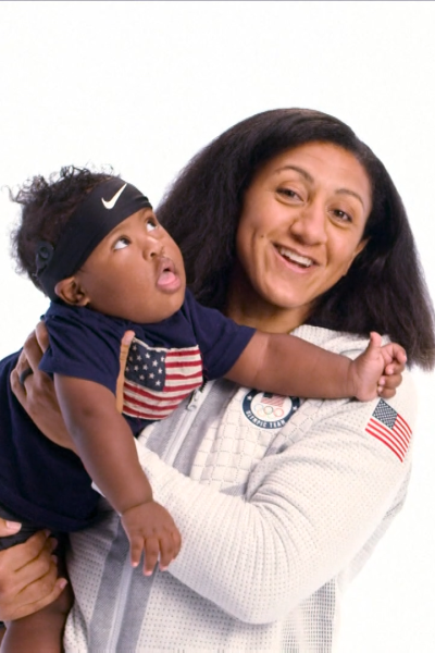 Three-time Olympic bobsled medalist Elana Meyers Taylor holds her baby next to her husband, smiling.