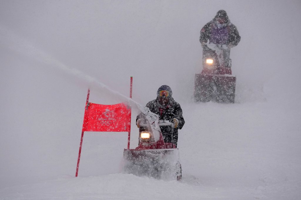 Course workers blow snow from the men's giant slalom course as the snow comes down at the alpine ski venue at the 2022 Winter Olympics, Sunday, Feb. 13, 2022, in the Yanqing district of Beijing.