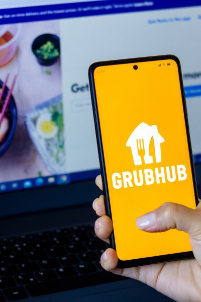 In this photo illustration, a woman holds a smartphone with the Grubhub Inc. logo displayed on the screen with the Grubhub website displayed in the background.