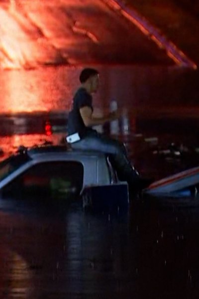 Man sits on top of truck stuck on flooded highway at night