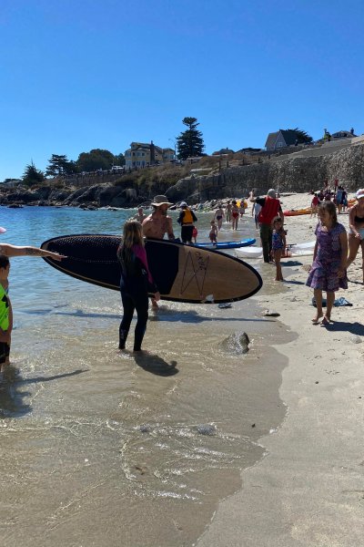 Paddle boarder standing on beach after attacked by shark holding a paddle board with bite marks