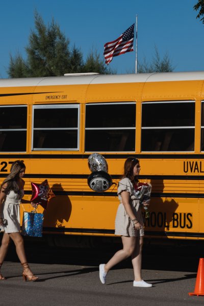 Students walking with balloons in front of yellow Uvalde CISD school bus.