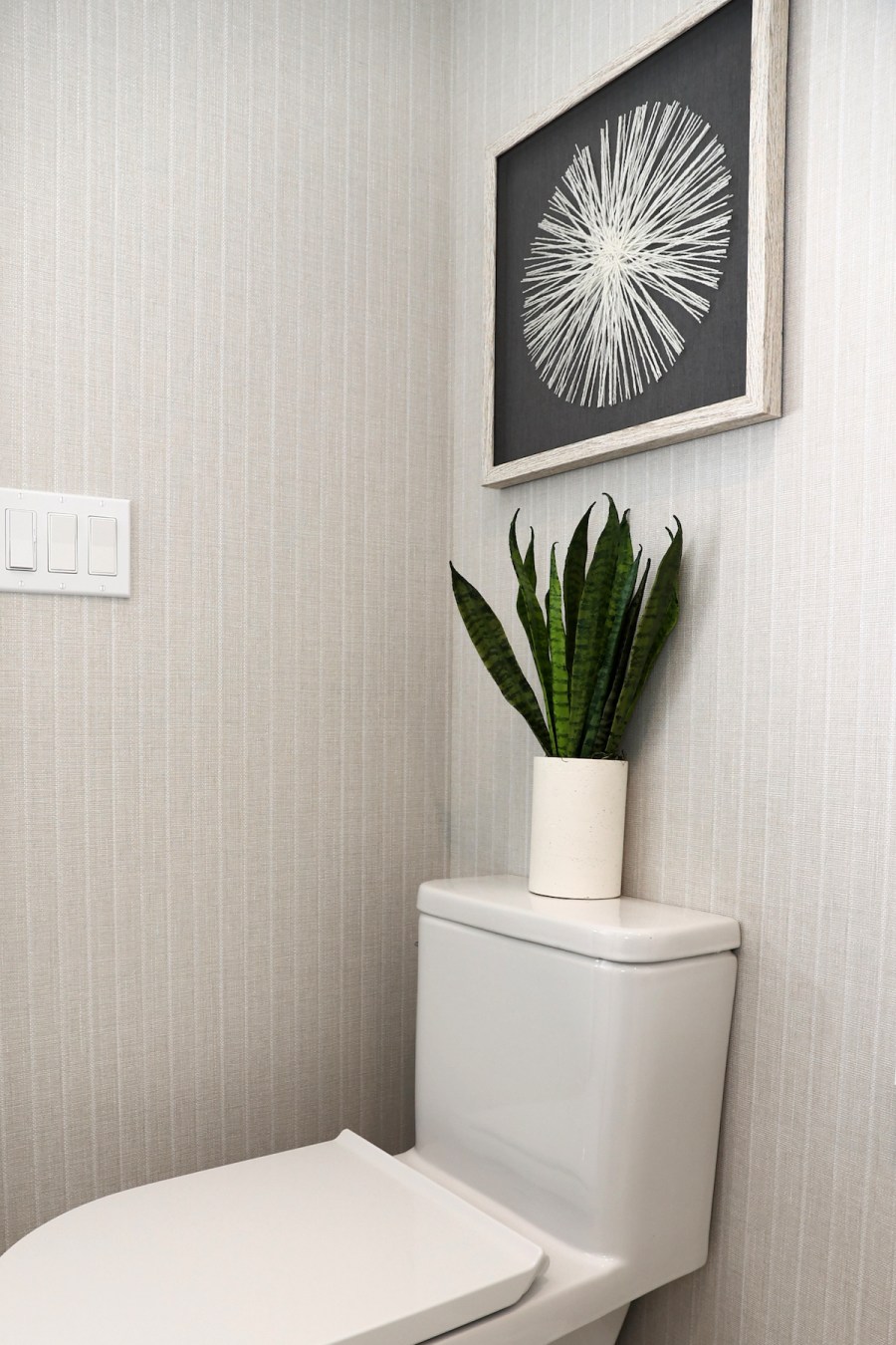 bathroom toilet with potted plant and art hanging over toilet